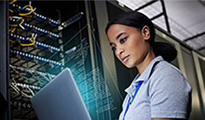 Stock image of female programmer in data server room working on a laptop.